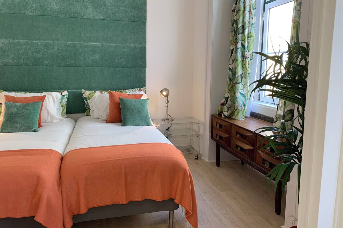 Une chambre avec deux lits, une tête de lit verte et une table de chevet en bois avec une lampe.