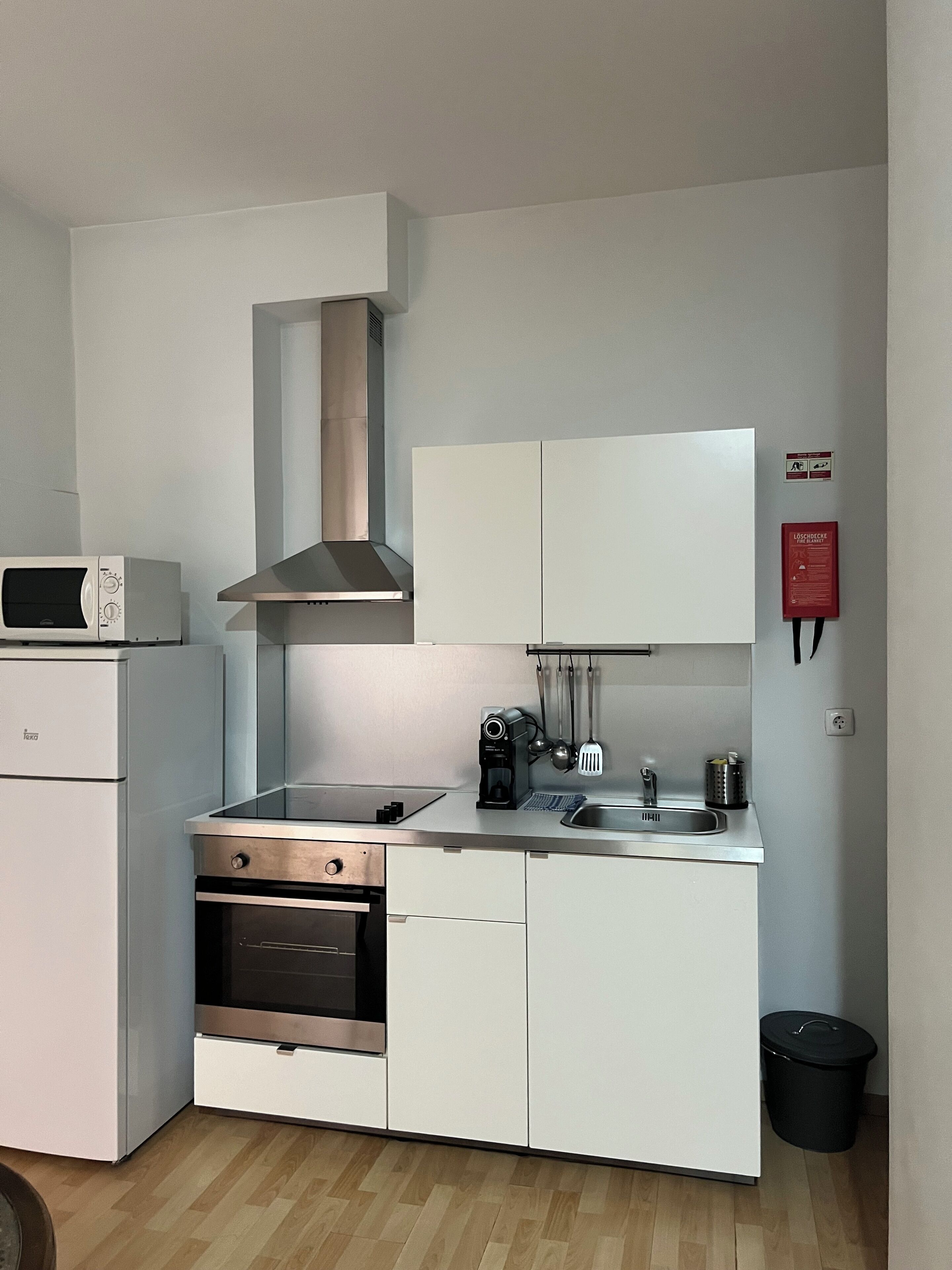 Une cuisine compacte équipée d’un four à micro-ondes, d’un four, d’une cuisinière et d’une hotte en acier inoxydable. On y trouve également des placards, un évier et une poubelle.