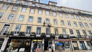 A multi-story building with balconies, storefronts including a souvenir shop and a cannabis store, and a pedestrian crossing. - Lisbon Heart (Lisbon)