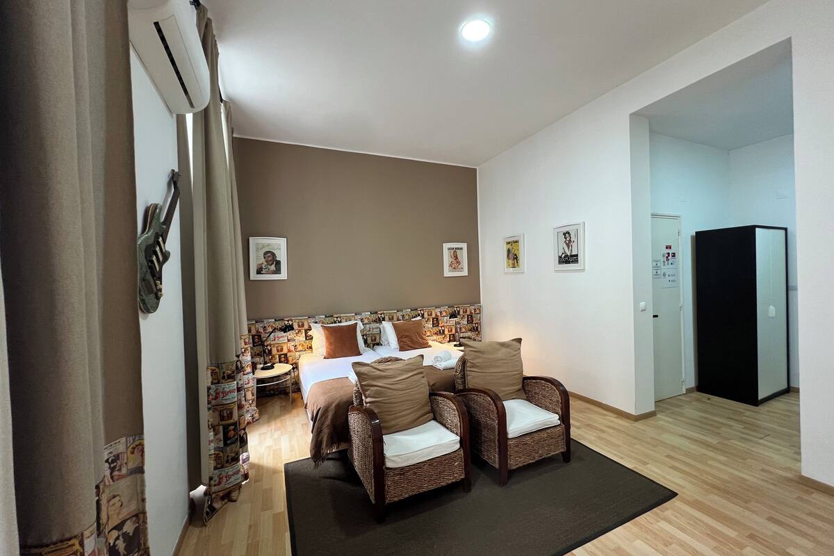Une chambre d’hôtel comprenant un lit, deux fauteuils en osier, une petite table, un bureau et un réfrigérateur.
