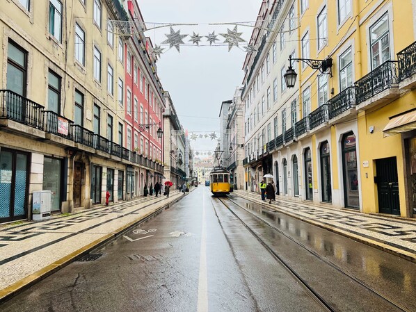 A tram on a wet street with buildings on either side, some with balconies and others with ground-level shops. - Lisbon Heart  (Lisbon)