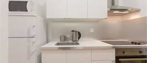 A modern kitchen with white cabinets, a built-in microwave, a kettle, and a stove.