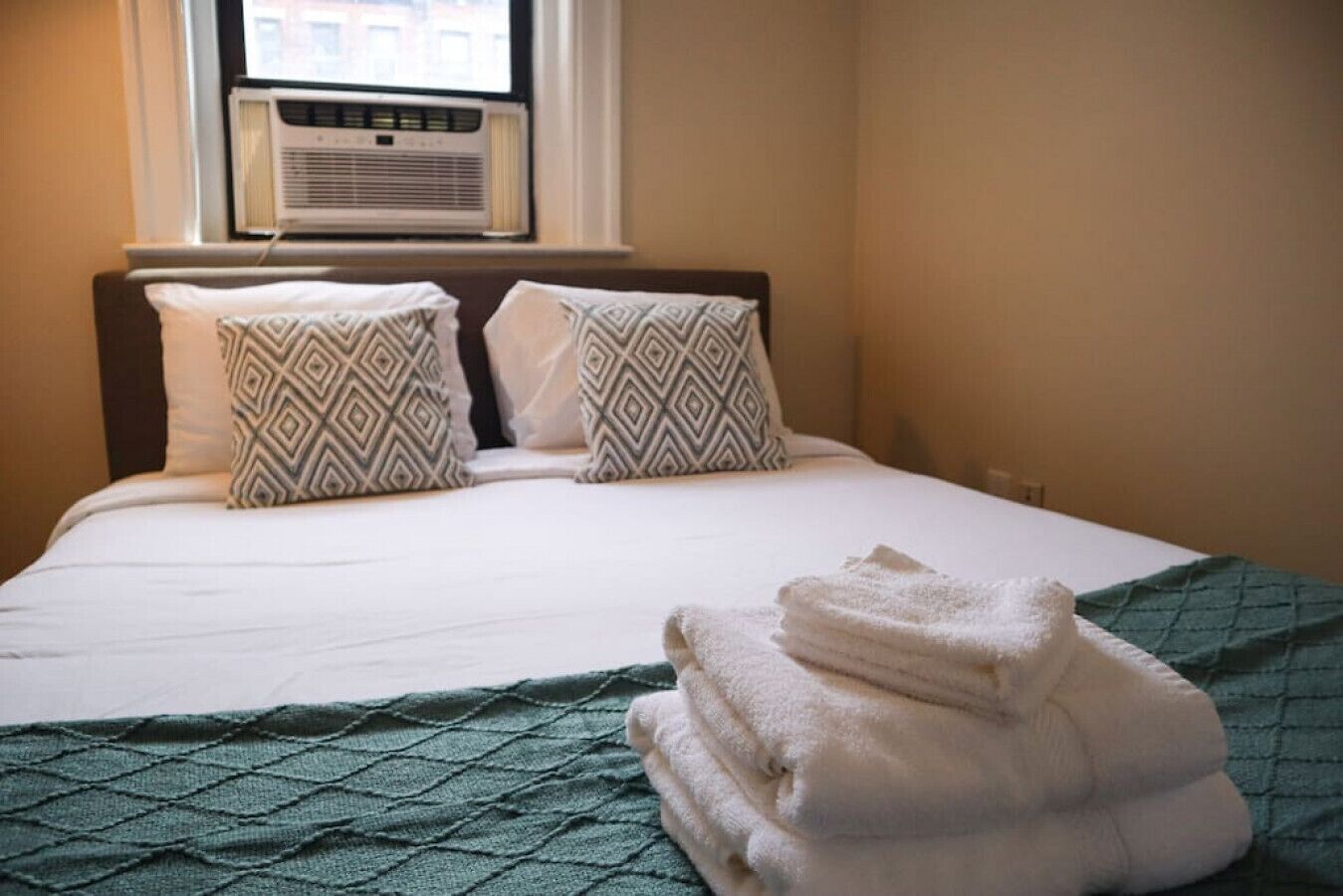 Uma cama bem arrumada com almofadas estampadas, um edredom verde e toalhas dobradas.