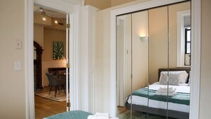 Une chambre d’hôtel comprenant un lit, un coin salon avec un fauteuil et un coin repas visible à travers une porte ouverte.