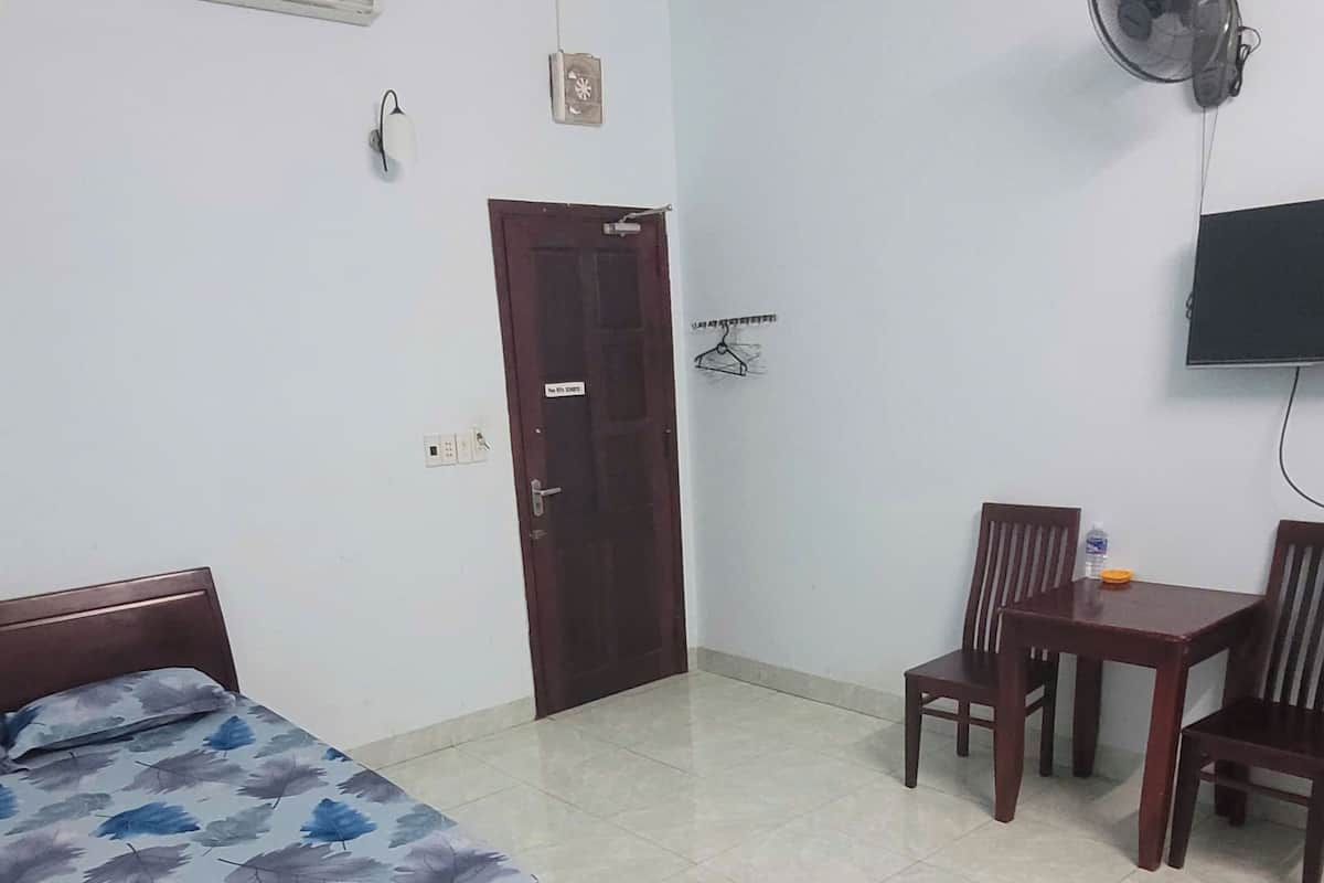 Una habitación con una cama, un escritorio con sillas, un televisor montado en la pared y un equipo de aire acondicionado.