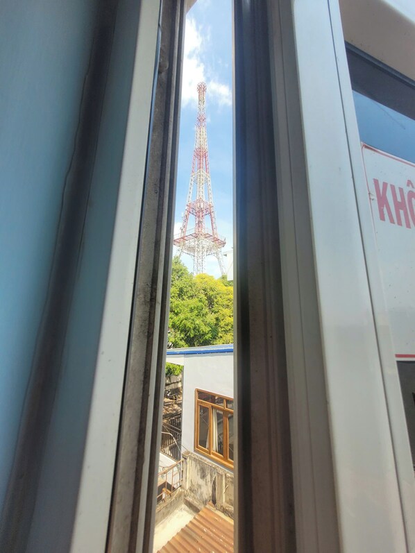 A view through a window of a building with a metal tower structure in the background. - Nha Nghi Tan Thanh 1 (Buon Ma Thuot)