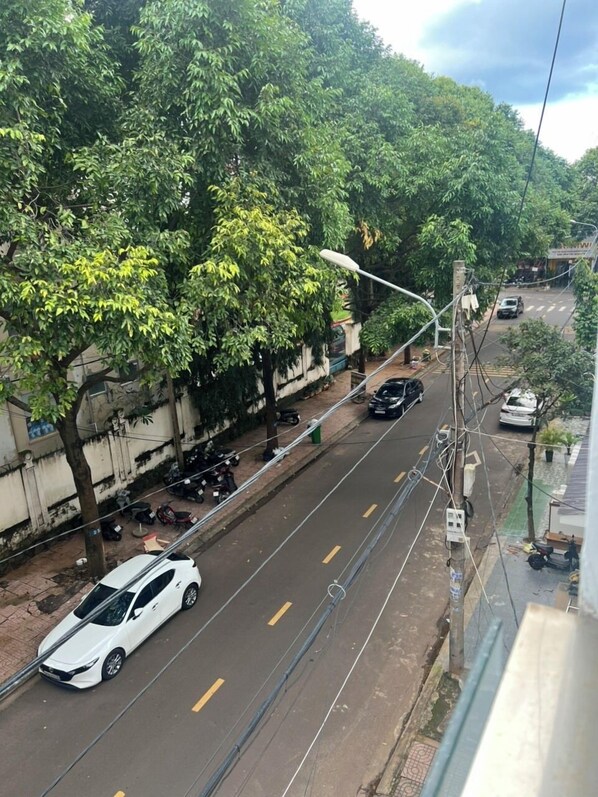 A street with a white car parked on the side, trees lining the road, and a pedestrian crossing. - Nha Nghi Tan Thanh 1 (Buon Ma Thuot)