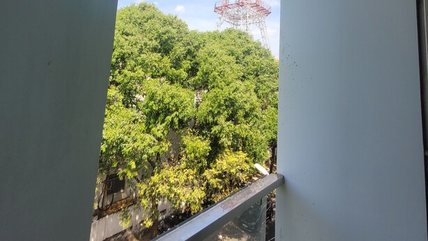 Vista de una alta torre de comunicaciones a lo lejos, un balcón con baranda metálica y una calle con coches estacionados.