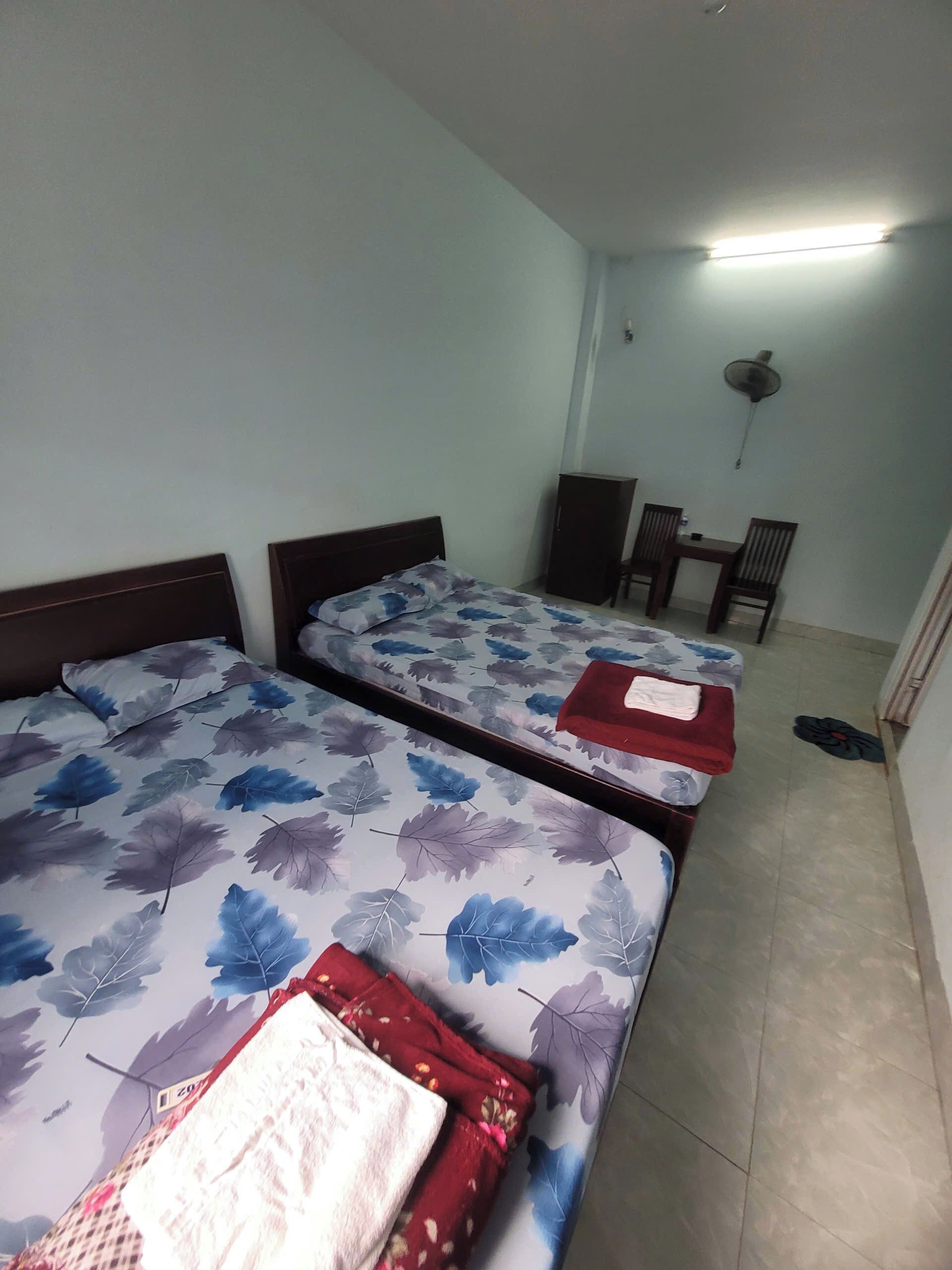 Ein Zimmer mit zwei Betten, einem Tisch, Stühlen, einem Ventilator und einem Fliesenboden.