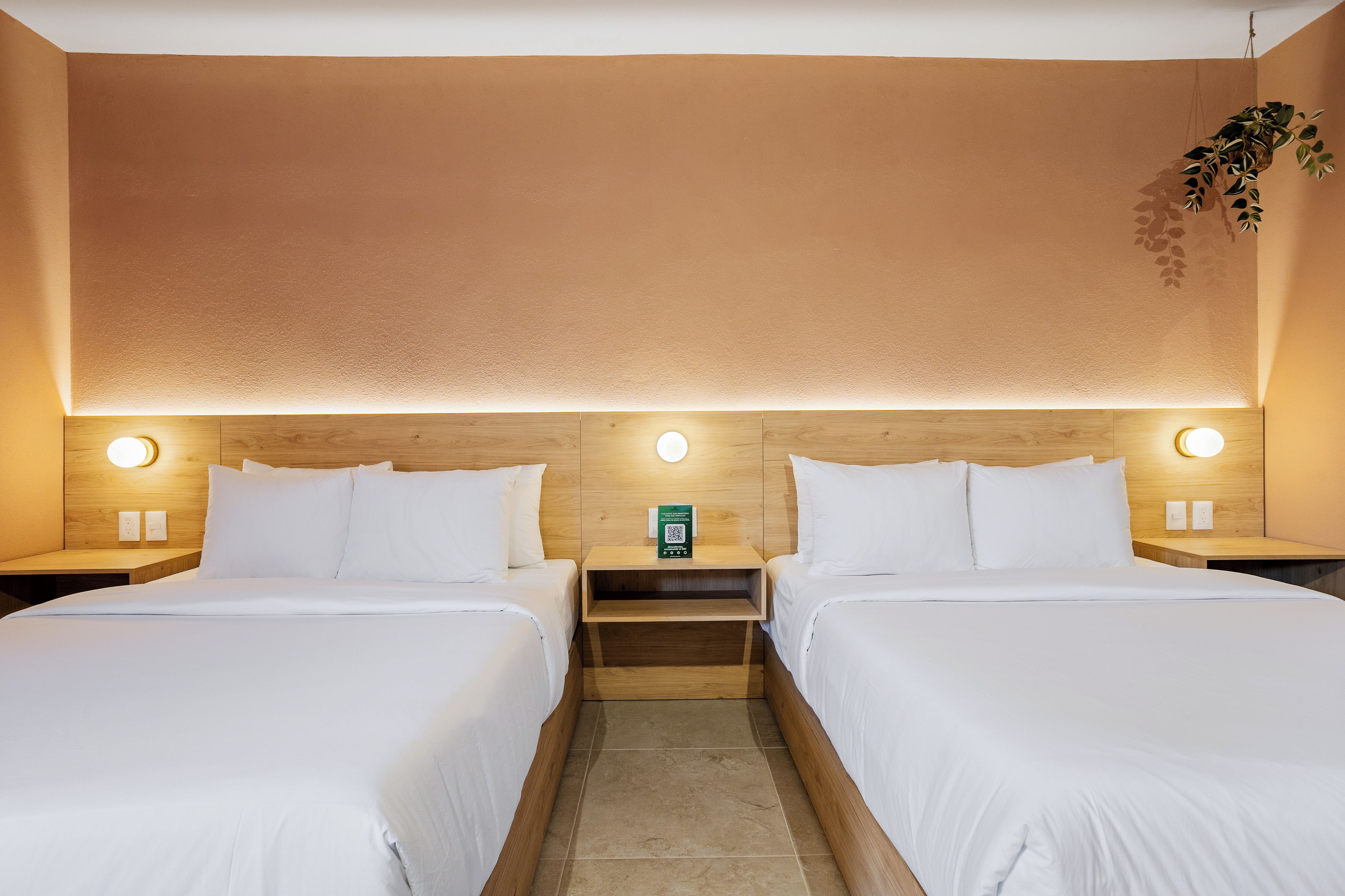 Habitación de hotel con dos camas, cabeceros de madera, mesitas de noche con lámparas y una pequeña mesita con un código QR.