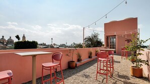 Eine Dachterrasse mit roten Metallstühlen und -tischen, Blumentöpfen und Lichterketten.