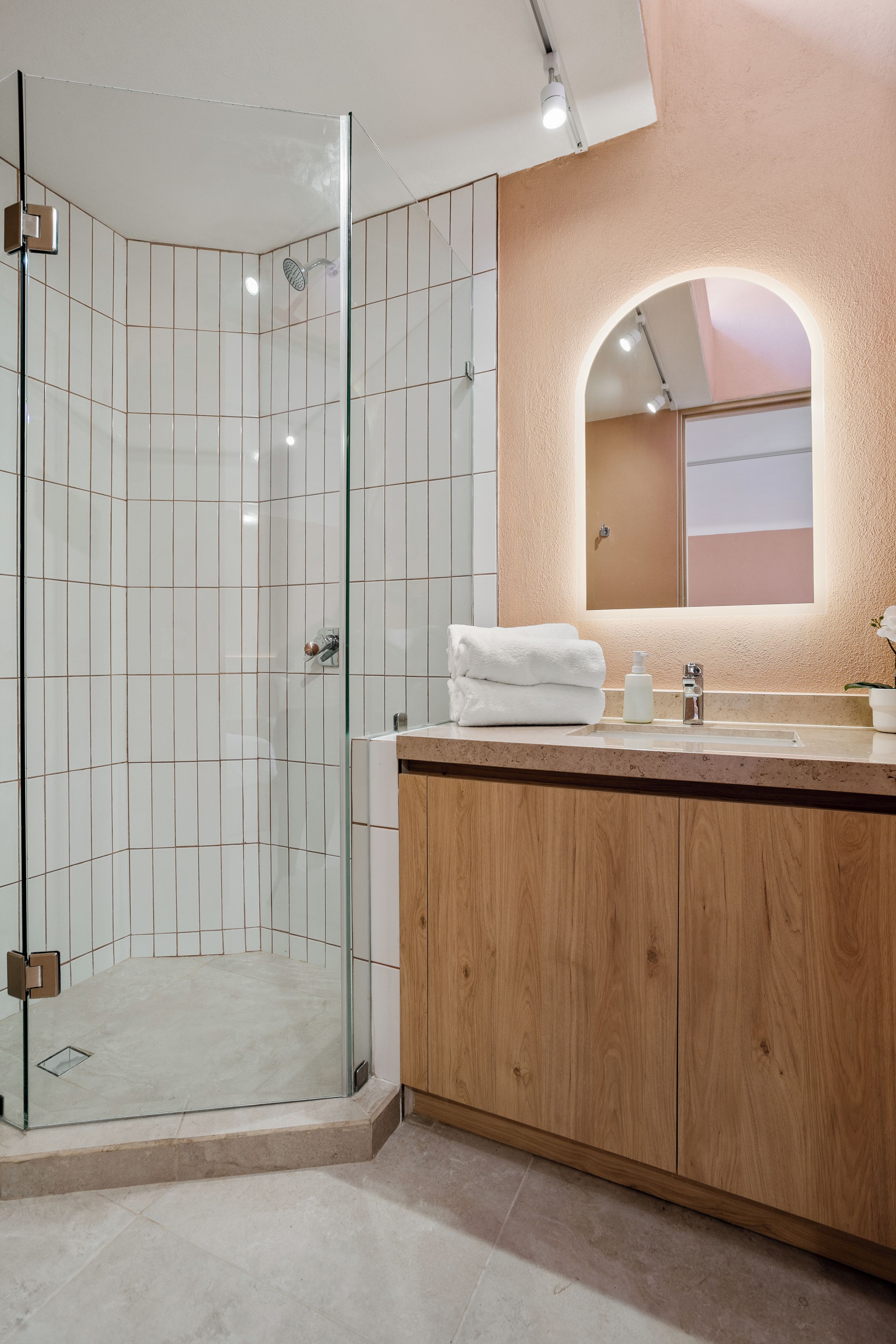 A modern bathroom with a glass-enclosed shower, a wooden vanity, and a mirror with an arched frame.