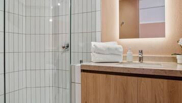 A modern bathroom with a glass-enclosed shower, a wooden vanity, and a mirror with an arched frame.