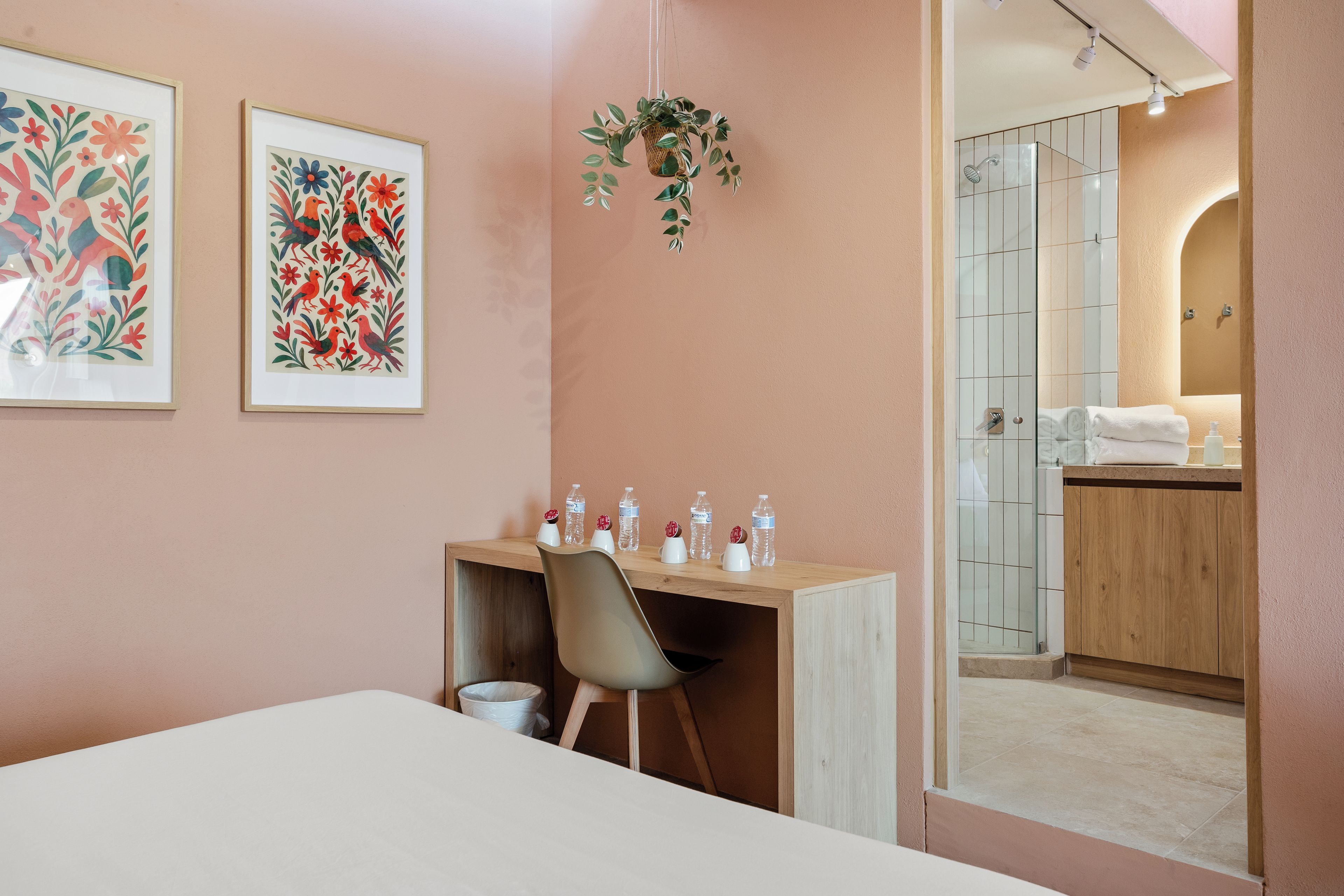 Une chambre d’hôtel avec un lit, un bureau et une chaise, une petite poubelle et une salle de bain visible à travers une porte ouverte.