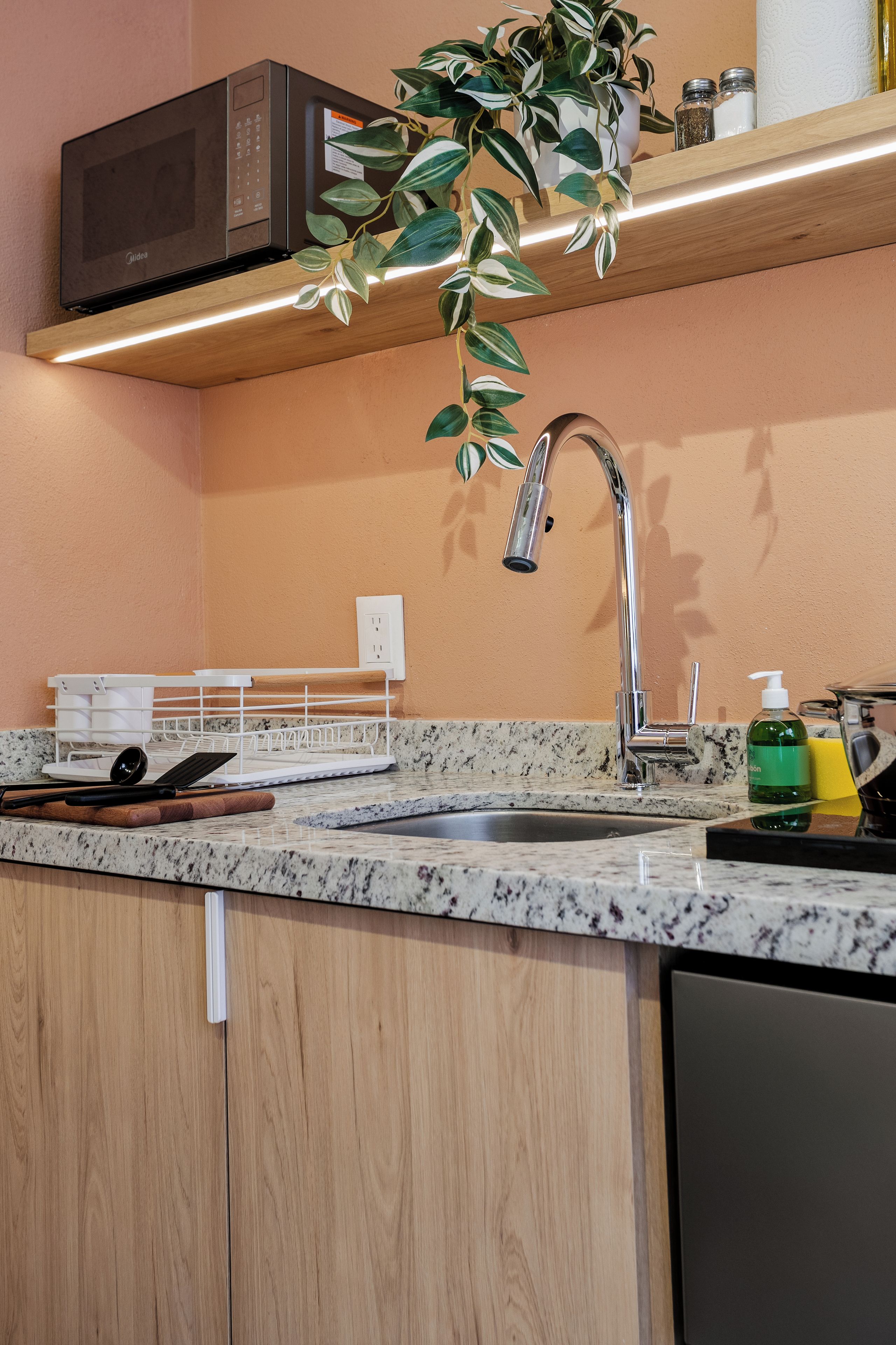 Una cocina con encimera de granito, pileta de acero inoxidable y un microondas arriba.