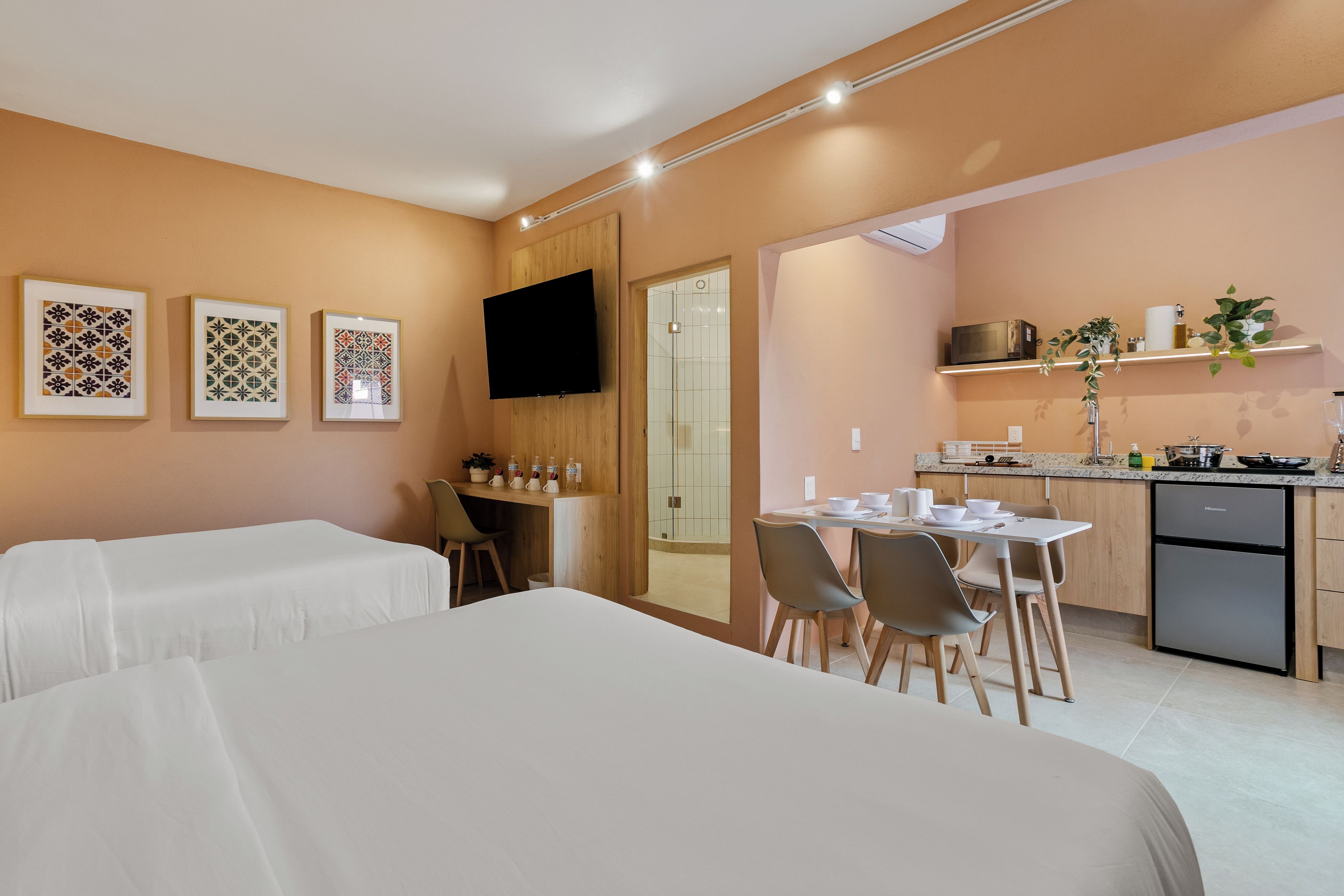 Une chambre d’hôtel avec deux lits, un coin repas comprenant une table et des chaises, une cuisine équipée d’un four à micro-ondes et un téléviseur fixé au mur.