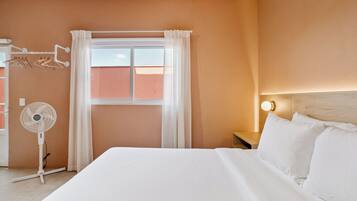 Una camera d'albergo con un letto, un comodino con lampada, una finestra con tende e un ventilatore a parete.