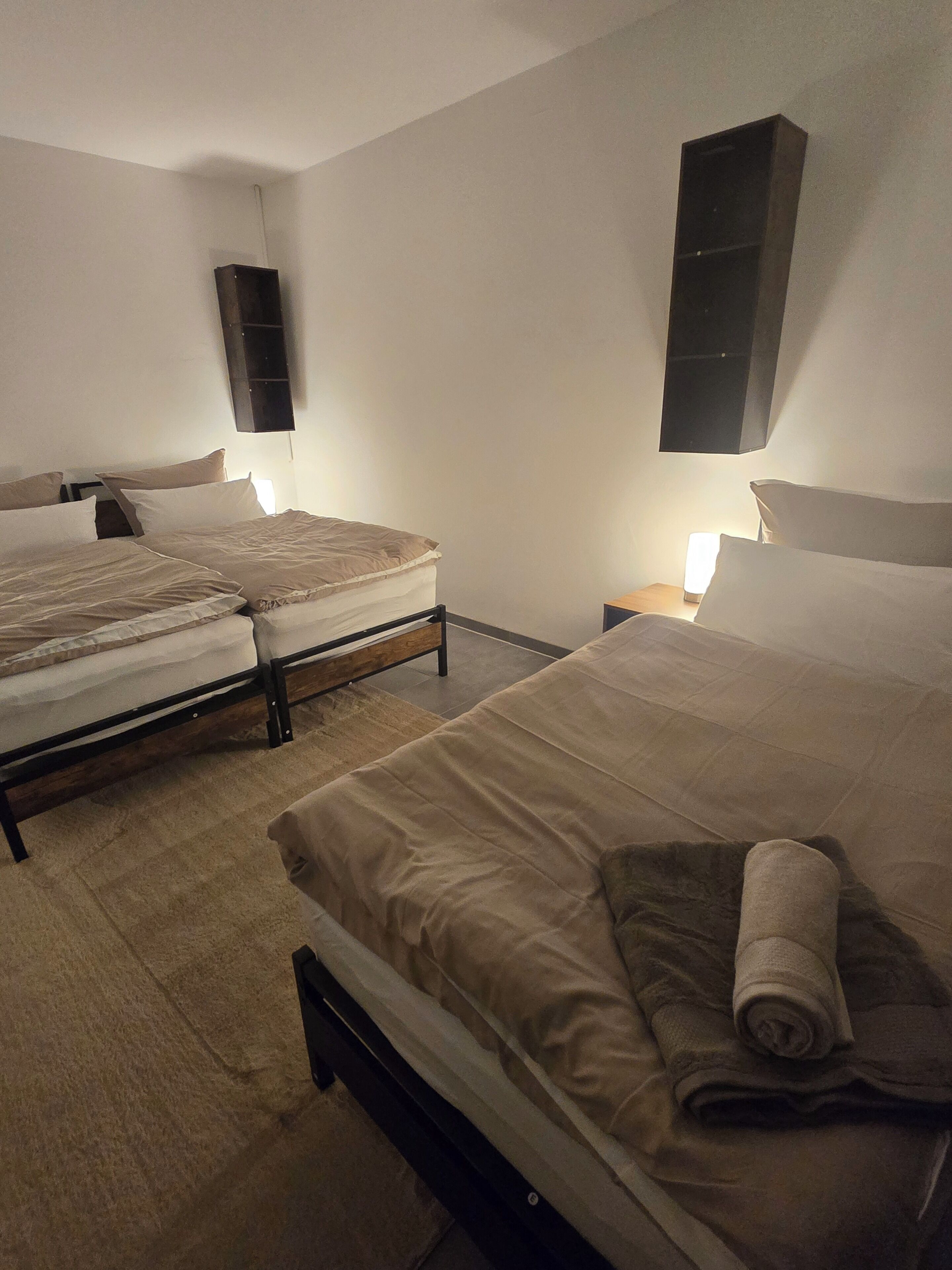 Ein Hotelzimmer mit zwei Betten, einem Flachbildfernseher, einem Nachttisch mit Lampe und einem an der Wand befestigten Lautsprecher.