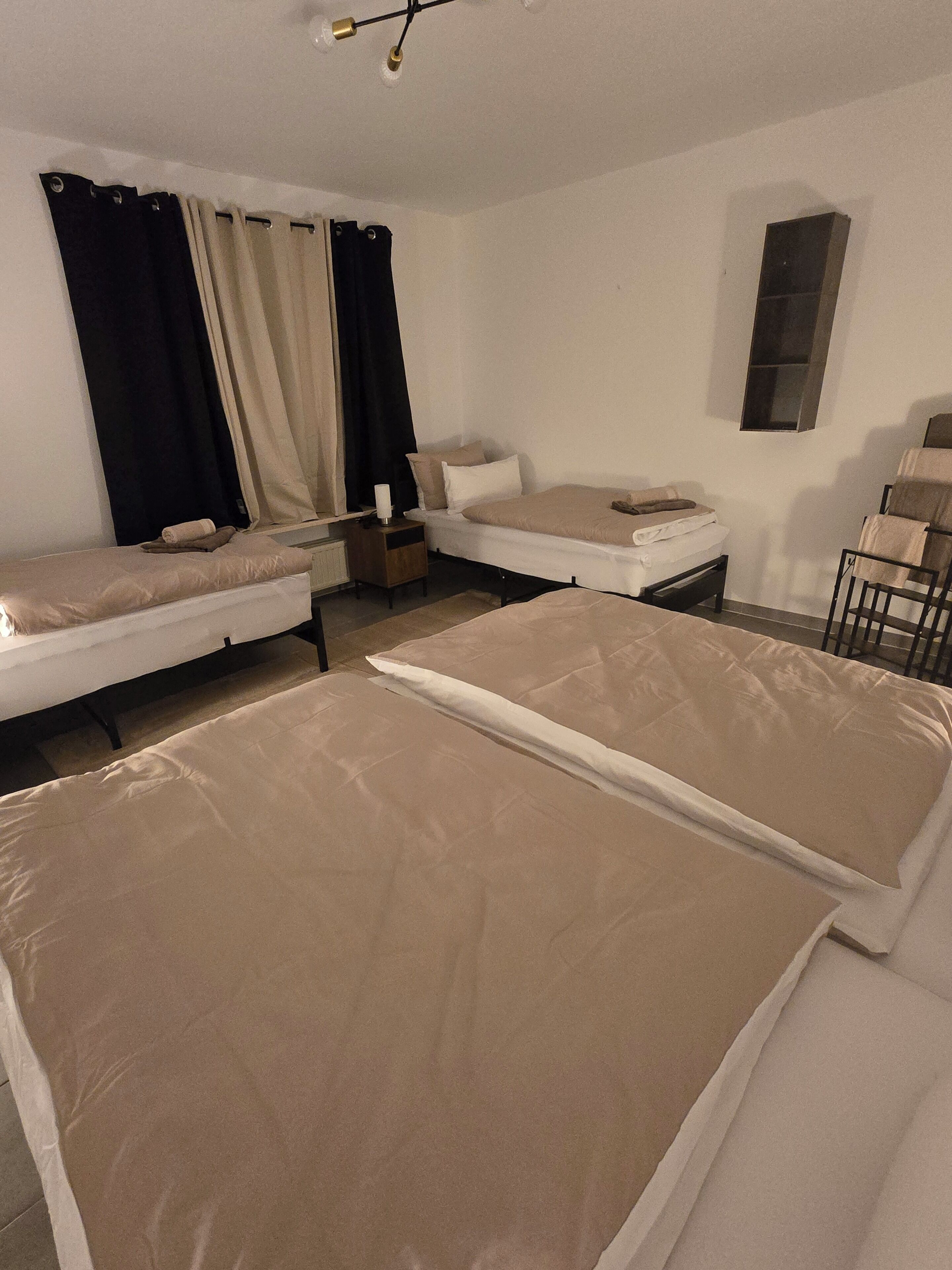Una habitación con dos camas, una mesita, una silla y una ventana con cortinas.