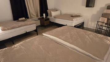 Una habitación con dos camas, una mesita, una silla y una ventana con cortinas.