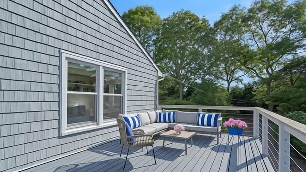 Een terras met een grijs geschubd huis, een wit raam en een blauw-witte gestreepte bank.