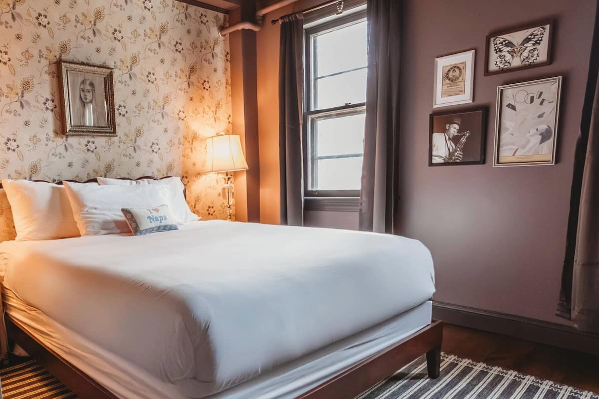 A neatly made bed with white linens, a bedside lamp, and a floral-patterned wallpaper.