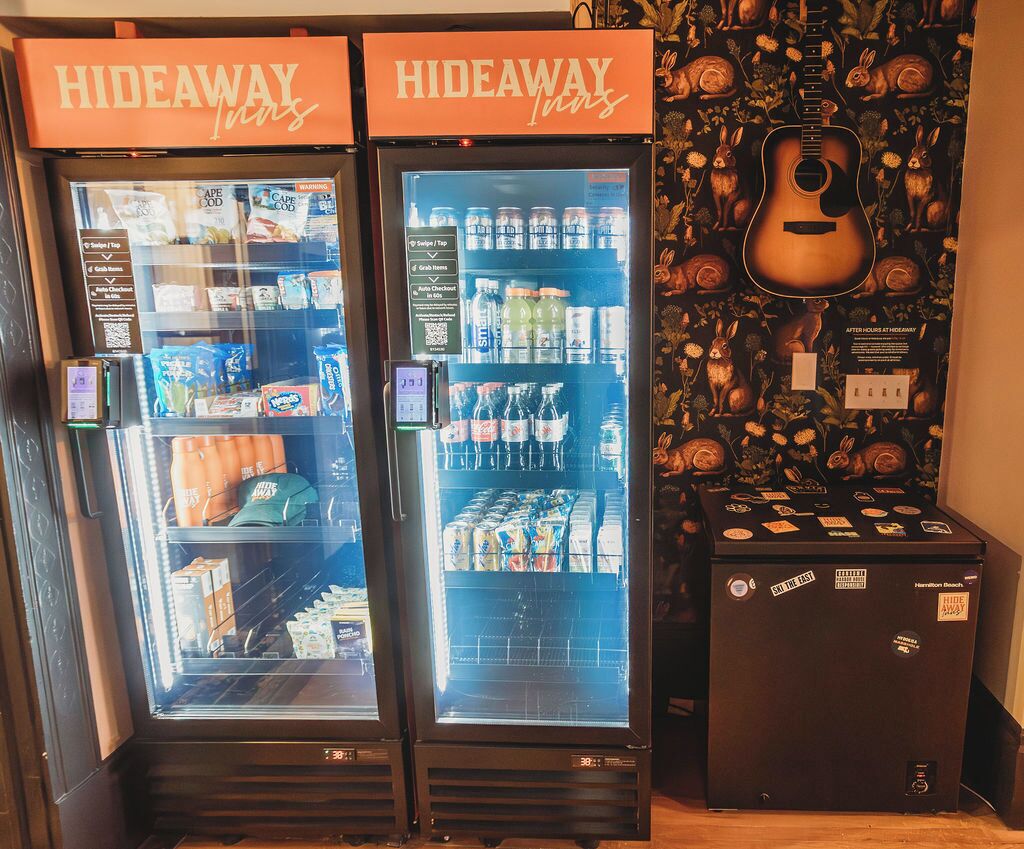 Duas máquinas de venda automática com a etiqueta 'Hideaway Inns', oferecendo diversas bebidas e lanches.