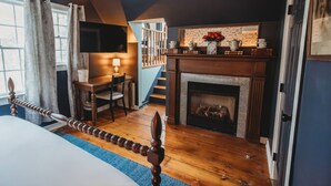 A bedroom with a bed, a fireplace, a staircase, and a TV mounted on the wall. - Hideaway Inn Lenox (Lenox)