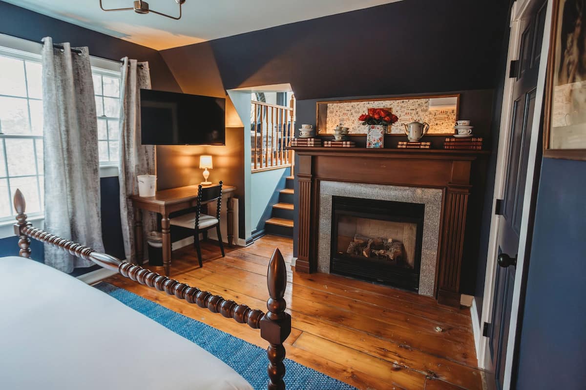 A bedroom with a bed, a fireplace, a staircase, and a TV mounted on the wall.