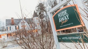 A sign for 'Hide Away Inn' with 'Hotel Entrance' below it, set against a snowy landscape with bare trees. - Hideaway Inn Lenox (Lenox)