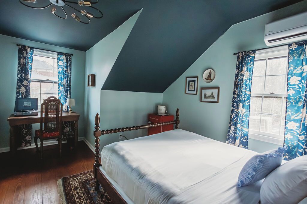 Un dormitorio con cama, escritorio, silla y ventana con cortinas.