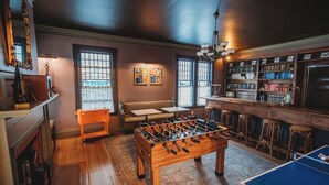 A room with a foosball table, a ping pong table, a bar area with stools, a fireplace, and a bookshelf. - Hideaway Inn Lenox (Lenox)