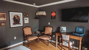 A room with a bed, two chairs, a small table, a television, and framed pictures on the wall.