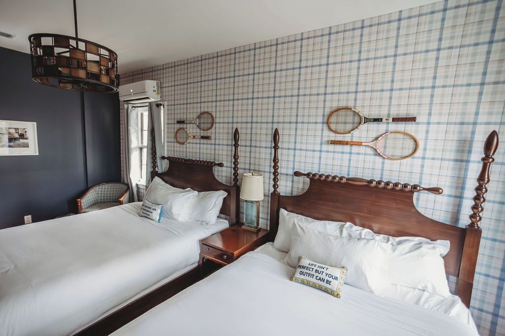 A hotel room with two beds, a wooden headboard, a checkered wall, and tennis rackets hanging on the wall.