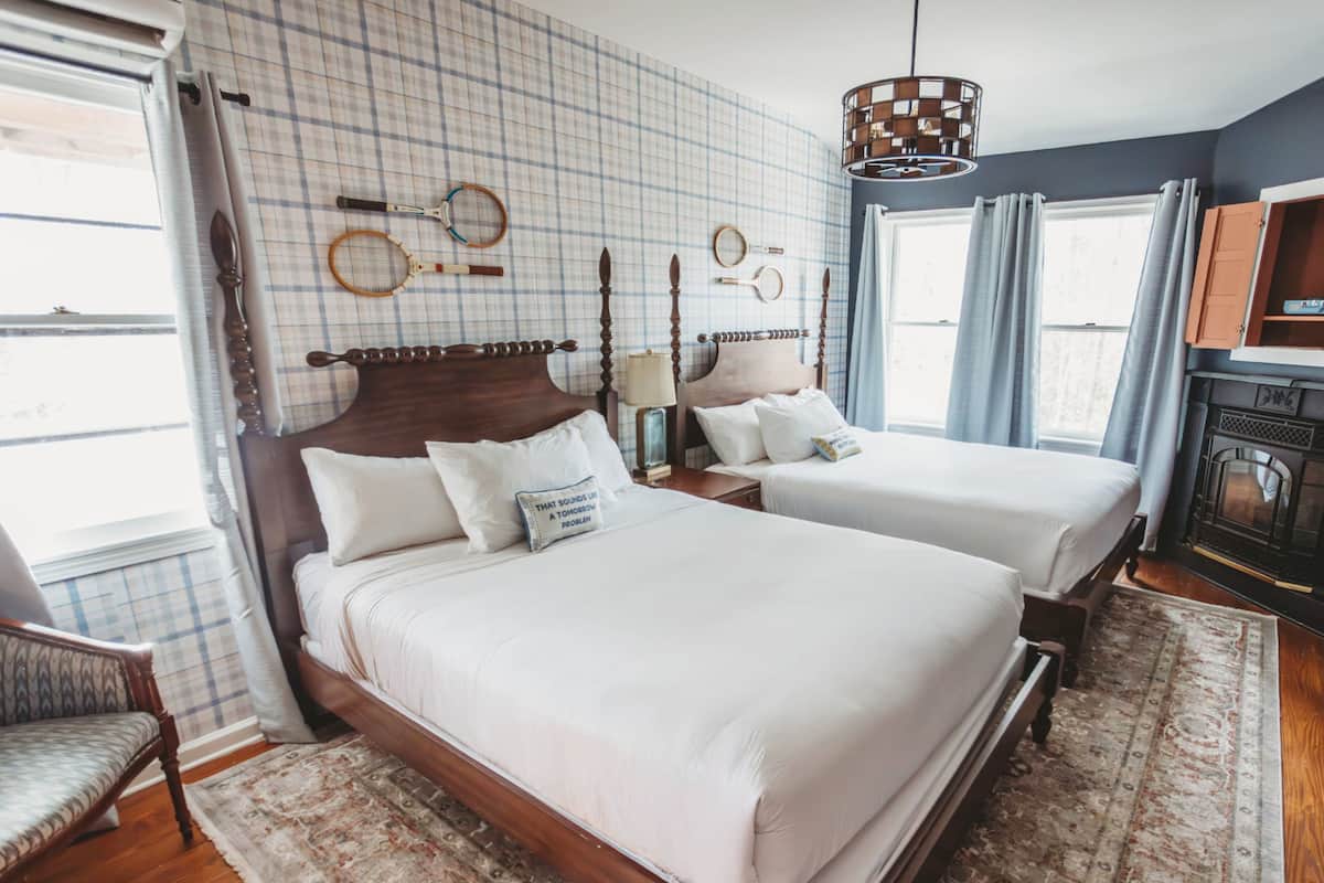 A double bed with a wooden headboard, a nightstand, a lamp, and a wall-mounted tennis racket rack.