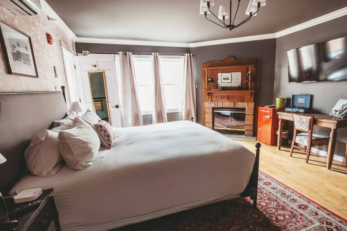 A bedroom with a large bed, a wooden headboard, a television, a desk, and a fireplace.