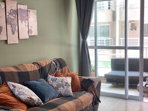 A living room with a sofa, pillows, a world map wall, and a view through a glass door. - BP03-Vento na Varanda Estilo Bali Lounge (Caucaia)