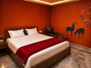 A room with a bed, a nightstand, a small table, and a wall with a deer mural. - ARYA RESIDENCY (Khandaparha)