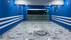 Ένας διάδρομος με μπλε τοίχους, μαρμάρινο δάπεδο και μια γυάλινη πόρτα στην οποία είναι γραμμένο το «ΚΑΛΩΣ ΟΡΙΣΑΤΕ».