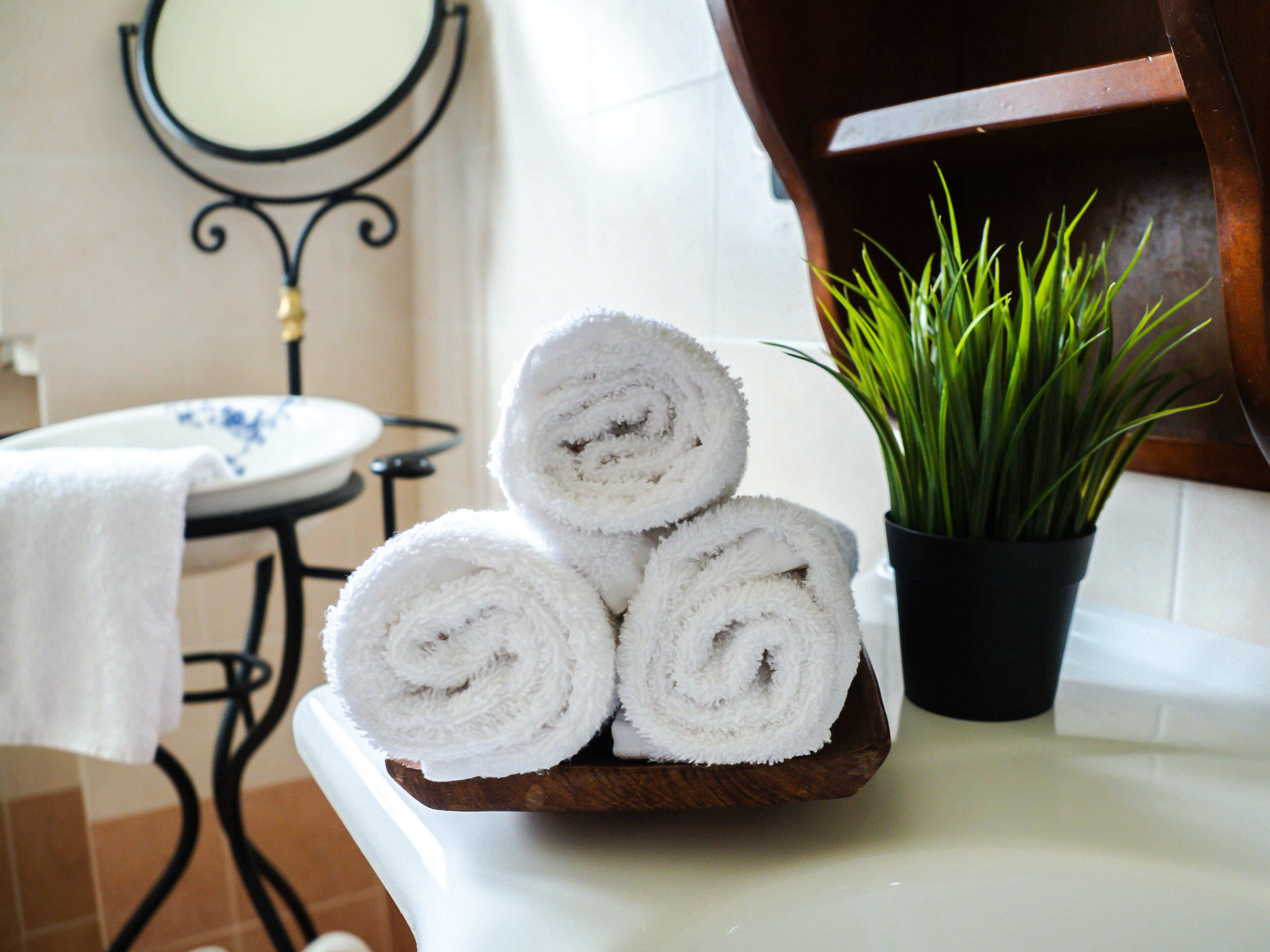A wooden tray with three rolled white towels on a white countertop.