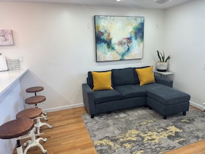 A modern living room with a grey sectional sofa, two mustard-colored cushions, a wooden coffee table, and a bar stool. - 2 Bedroom Apartment Suite  in Quiet Neighborhood (Hempstead)