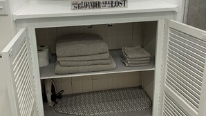 A white shelf with a potted plant and a sign that reads "not all wanderers are lost." Below, there are towels and a patterned mat. - 2 Bedroom Apartment Suite  in Quiet Neighborhood (Hempstead)