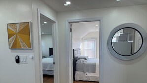 A hallway leading to a bedroom with a bed, a round mirror, and a wall-mounted picture. - 2 Bedroom Apartment Suite  in Quiet Neighborhood (Hempstead)