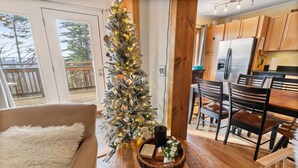 A cozy living room with a wooden dining table, a fluffy white chair, and a decorated Christmas tree. - Summit 104D Beautiful 3BR, 2BA condo in The Summit at Snowshoe (Snowshoe)