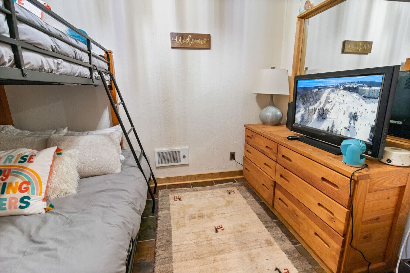 Ett rum med våningssängar, en tv, en byrå i trä och en skylt med texten ”Välkommen”.