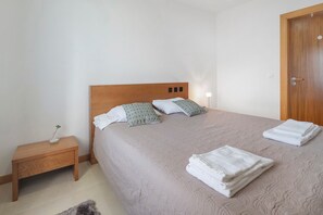 A neatly made bed with a headboard, a bedside table with a lamp, and a door to the right. - Apartment 'Quinta Da Faya' with Sea View, Balcony and Wi-Fi (Angra do Heroísmo)