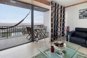 A living room with a glass coffee table, a black leather sofa, a dining table with chairs, a hammock, and a view of the ocean. - Apartment 'Quinta Da Faya' with Sea View, Balcony and Wi-Fi (Angra do Heroísmo)