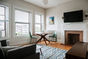 A modern living room with a fireplace, a dining table, and two chairs. - Cozy 1BDR Close to Fenway! (Boston)