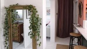 Una habitación con un espejo rodeado de hiedra, una cortina marrón y un pequeño taburete.