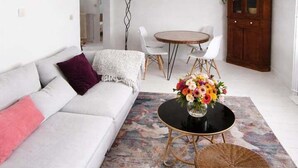 Una sala de estar moderna con un sofá, una mesa redonda con sillas, una mesa de centro de mimbre y un jarrón decorativo.